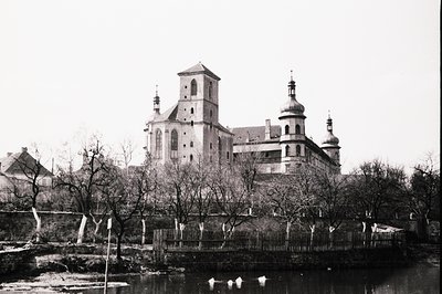 Opulent Baroque architecture dominates this view. A large monastery or palace complex features a central tower and distinctiv...