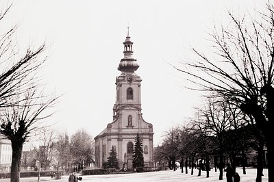 A stately church dominates the view, featuring a distinctive tiered tower with a spire. Flanked by bare trees lining a wide, ...