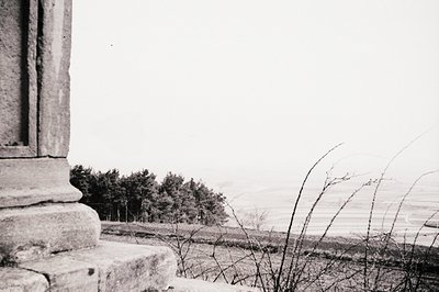 Detailed architectural detail of a stone ledge frames a landscape vista. Sparse vegetation and low-lying trees are visible in...