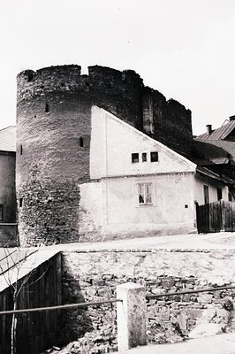 Stone tower, likely defensive in origin, stands adjacent to a white-walled building with arched windows. A weathered stone wa...