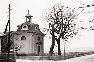 Monochromatic view of a small, ornate chapel with a domed roof and bell tower. Stone architecture, arched doorway, surrounded...