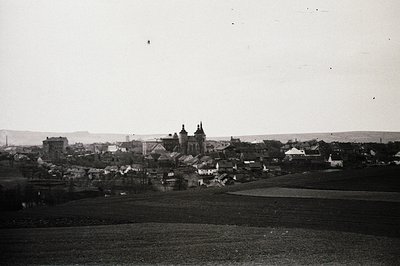 <start_of_image>High-angle view of a town, dominated by a church with twin towers, nestled within rolling hills. Buildings di...