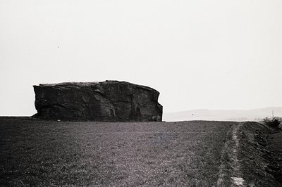 Striking monochrome image of a solitary, weathered rock formation rising from a gently sloping landscape. The rock's layered ...