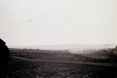 A long view of rolling hills and a distant town, captured in a vintage black & white photograph. Sparse vegetation covers the...