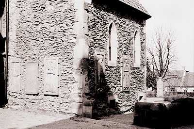 A stone building with Gothic Revival windows and a weathered appearance. Likely a church or public structure, with a partiall...