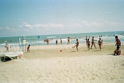 A candid snapshot of a seaside beach scene. Several people are playing volleyball on the sandy shore. A lifeguard station and...