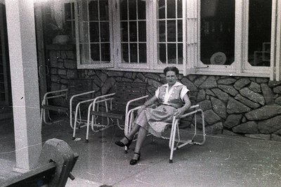 A young woman seated in a folding chair within a stone-walled courtyard. Architectural details show a stylized design with a ...
