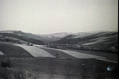 A wide, sweeping view showcases rolling hills and terraced farmland, possibly in the English countryside. Visible crops indic...