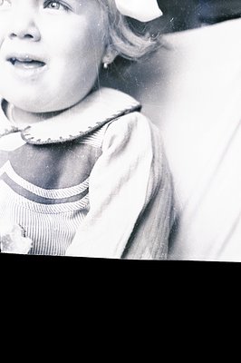 Close-up black and white portrait of a young girl with blonde hair, wearing a striped sailor style shirt. Likely a candid sna...