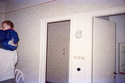 A young child, swaddled in a blue jacket with patterned graphics, is held by an adult's arm. The photo captures a domestic in...