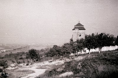 A stone tower stands prominently amidst a landscape of rolling hills and a distant horizon. A dirt path leads uphill to the t...