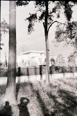 A modernist villa, likely residential, features clean lines and geometric forms, set against a backdrop of foliage and a ston...