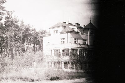 A large, three-story villa with multiple windows and a steeply pitched, tiled roof. Situated within a wooded area, the struct...