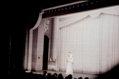 A stage scene features a draped backdrop and classical architectural details – arched doorway flanked by pilasters. A perform...