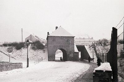 Exterior view of a stone gatehouse, possibly a former military or coastal fortification. Heavy snowfall covers ground and veg...