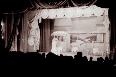 Stage scene depicts a theatrical performance, possibly a ballet or opera. Elaborate backdrop features architectural details; ...