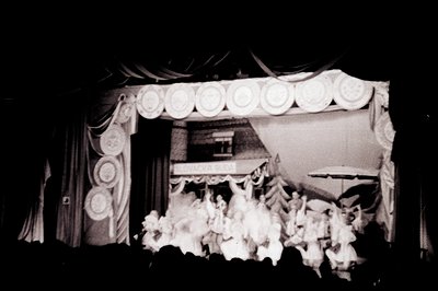 Stage scene captures a performing arts group, possibly ballet or folk dance, amidst draped backdrop and detailed stage décor....