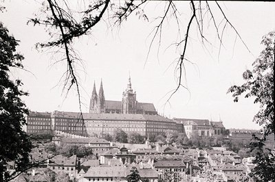 A high-angle view captures Prague Castle, distinguished by its Gothic cathedral spires, rising above a densely packed citysca...