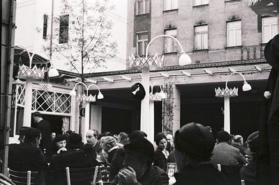 A view of a cafe courtyard, likely in Eastern Europe. Patrons seated at tables beneath a decorative colonnade with a prominen...