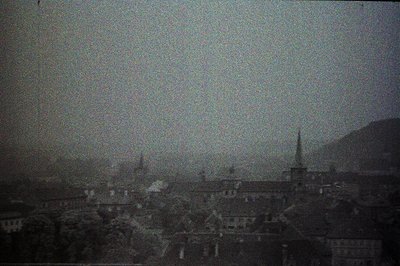 A panoramic, grainy view depicts a European cityscape with numerous rooftops and several prominent church spires rising above...