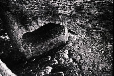 Arched stone structure, likely a bridge or viaduct, overlooks turbulent whitewater. Detailed stonework exhibits considerable ...