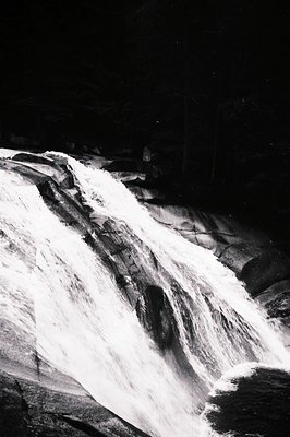 Dramatic black and white image capturing cascading water over rugged rock formations. Likely a waterfall scene, with dense fo...