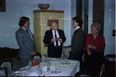 Three men and a woman stand near a table set for a formal dinner. The room features a decorative brick fireplace. Dress code ...
