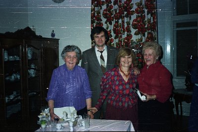 A family portrait captured indoors; four individuals stand near a table laden with a tiered cake, likely a celebration event....