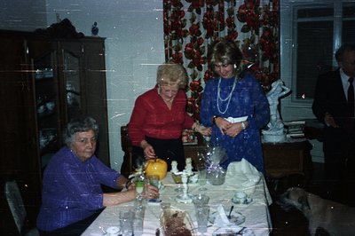 Festive gathering featuring three women and a man seated around a formally set table with crystal glassware & floral centerpi...