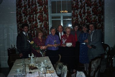 Formal portrait of seven people and a dog seated at a decorated table. Likely a celebratory occasion with floral arrangements...