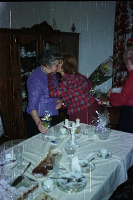 Warm, candid moment depicting a hug between two individuals indoors. Festive decorations and a formal dining table with glass...