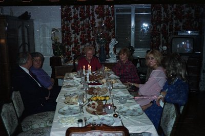 A family gathers around a lavishly set table, likely for a holiday meal. The dining room showcases a 1970s aesthetic: pattern...