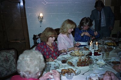Candid snapshot of a formal dinner party, possibly a holiday celebration. Four women and one man are seated around a laden ta...