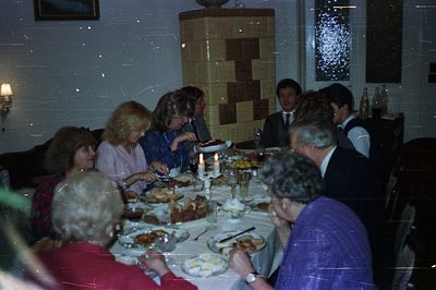 A lively family gathering centered around a bountiful table laden with food. Individuals in formal wear appear engaged in con...