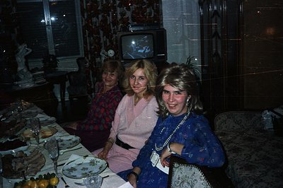 Three women seated at a lavishly set table; likely a celebratory dinner. Interior shows dated decor, including a vintage tele...