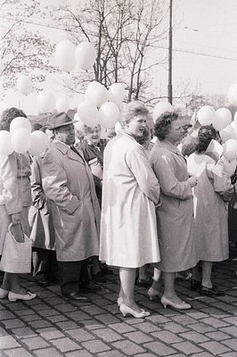 Group portrait of six individuals in overcoats, amidst a release of white balloons. Appears to be an outdoor event, likely a ...