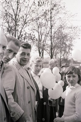 Group portrait capturing a mid-century moment: a man in a double-breasted coat stands prominently alongside women and childre...
