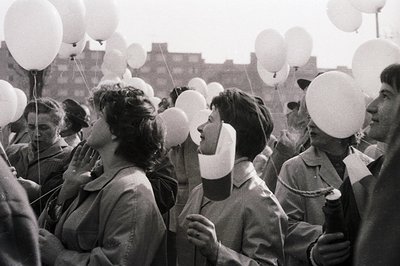 Crowd gathered, releasing white balloons – potentially a memorial or celebration. People wear vintage clothing, some in milit...