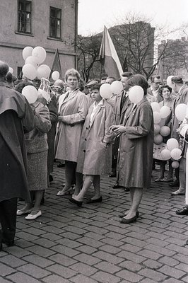 Group photo from the 1960s showing a crowd, likely at a public event. Individuals wear trench coats & carry white balloons; s...