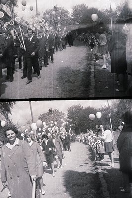 Group of children and adults march along a tree-lined road, carrying sticks with attached decorations and balloons. A man in ...