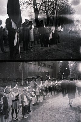 A community gathering features children in costumes lining up, possibly for a parade or ceremony. Several men in suits hold f...