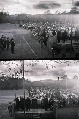 Large gathering observed on an outdoor platform overlooking a scenic landscape. Individuals in uniform stand guard beside a s...