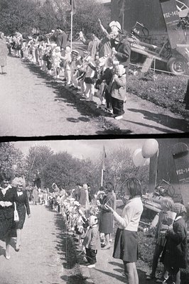 Children march in a procession alongside a military vehicle (labeled "VSZ-14") with a formal air. Numerous dolls are carried ...