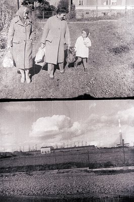 Three figures – two women and a child – walk across a grassy area, carrying bags. The women wear long coats and hats, typical...