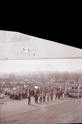 Vintage image: outdoor gathering featuring uniformed marchers carrying flags, likely a parade or commemorative event. Trees &...