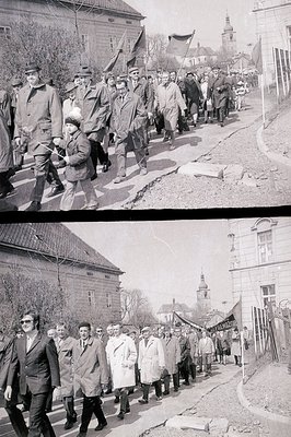 A group marches across a crosswalk, apparently in a formal procession. The subjects are predominantly men in overcoats and ha...