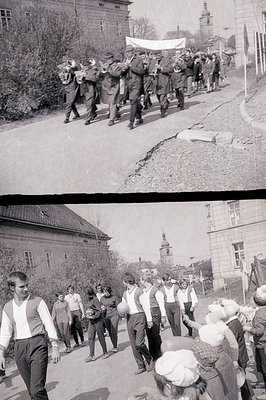 A marching band procession ascends a sloped street, likely during a festival or parade. Musicians carry brass instruments and...