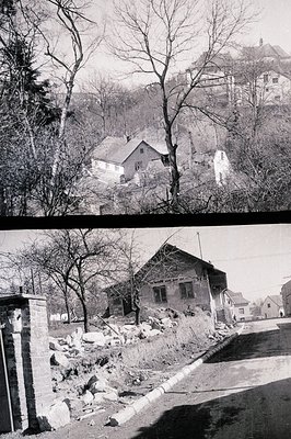 A view of a traditional, steeply-roofed house nestled into a wooded hillside, possibly an alpine region. The image presents a...