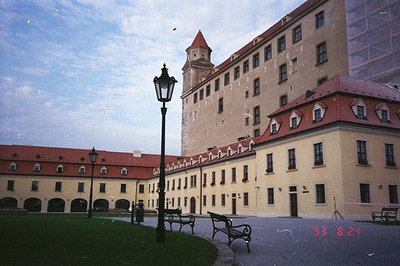 Grand, cream-colored architecture dominates this view. A central castle rises above a surrounding, lower complex with arched ...