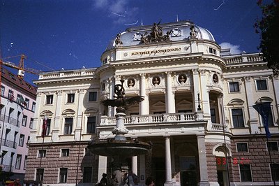 Elegant, Neo-Baroque theater facade with a central fountain featuring a winged statue. “Slovenske Narodne Divadlo” is inscrib...
